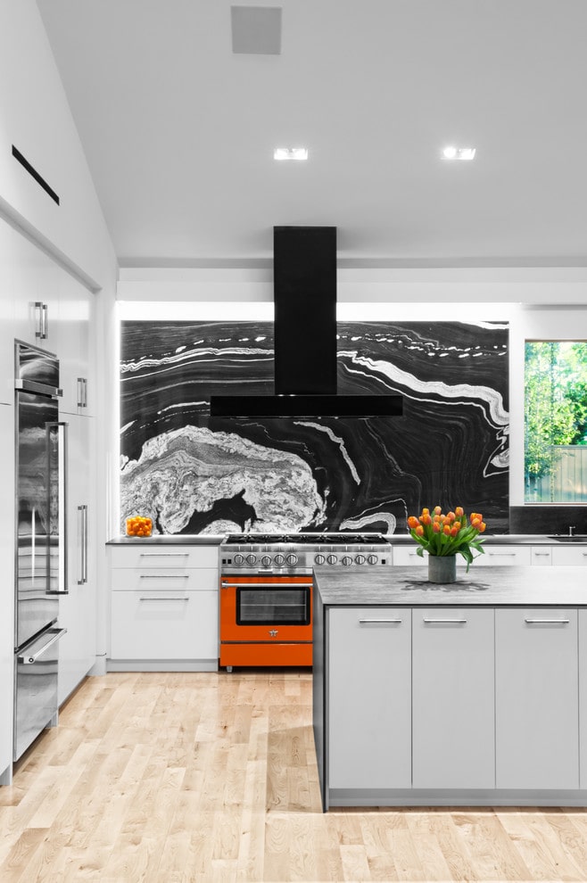 Black and white kitchen with stone slab backsplash and red oven.