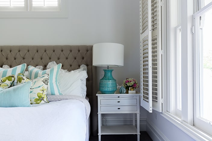 Coastal bedroom with tufted headboard and wooden shutters.