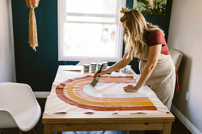 Pregnant woman painting rainbow on canvas.
