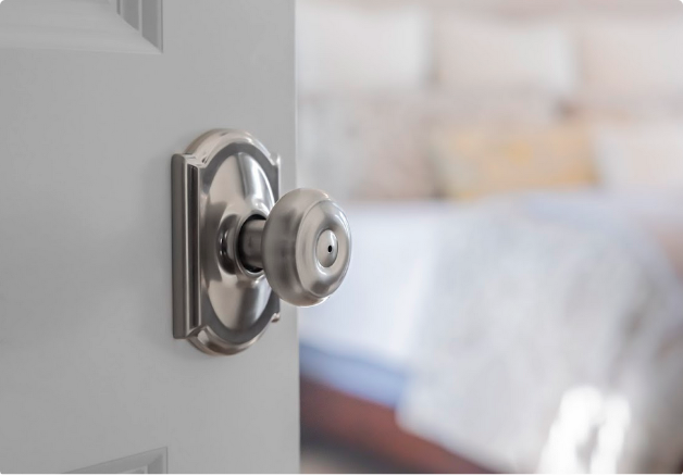 Close up of a tradtionally door knob on a bedroom door withe a bed in the background 